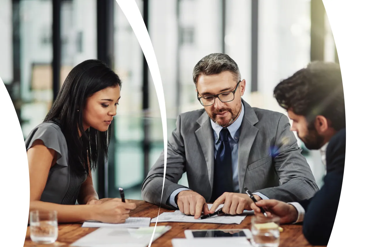 Three business professionals collaborating at a table, reviewing documents and discussing strategy.