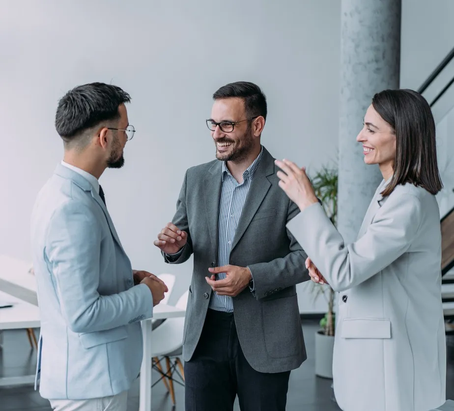 Three professionals in suits smiling and talking in a modern office