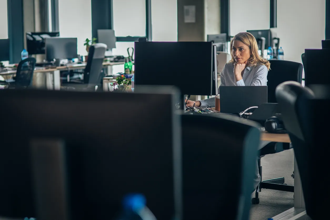 A woman working on a laptop in a spacious office with multiple desks and monitors