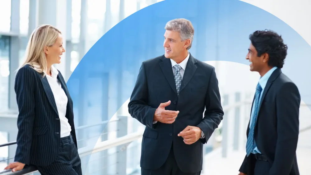 Three business professionals having an animated discussion in a bright modern office hallway