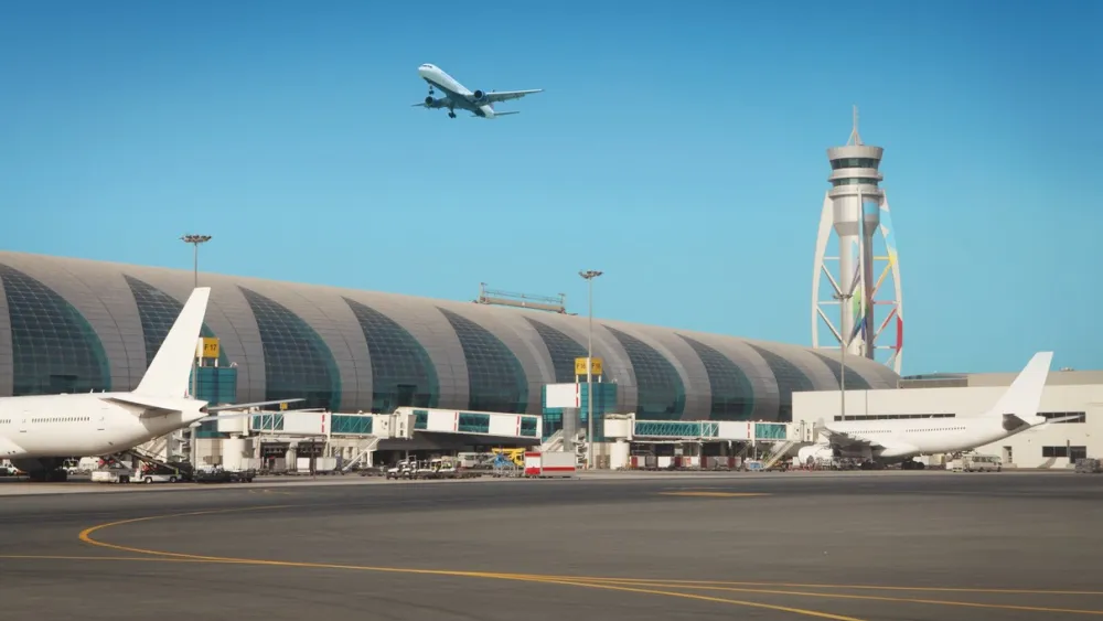Airport runway with planes parked and control tower under clear blue sky