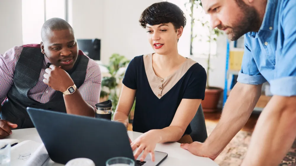 Three colleagues collaborating at a desk with a laptop in an office