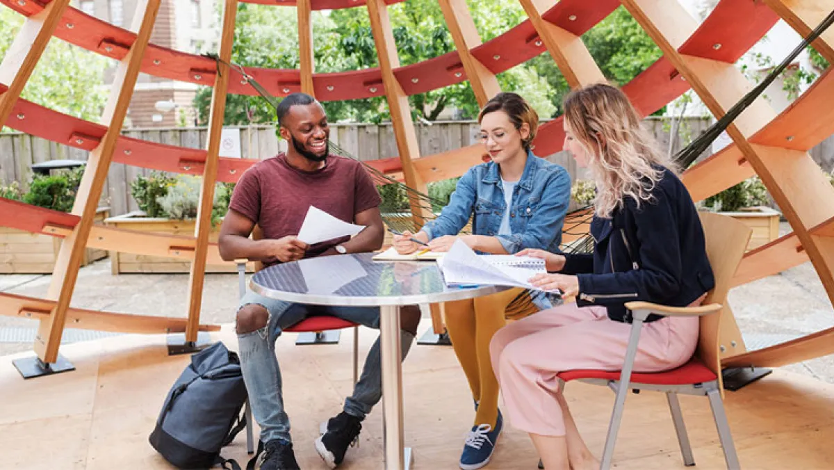 3 students sat at a circular glass table with an abstract wooden object behind them
