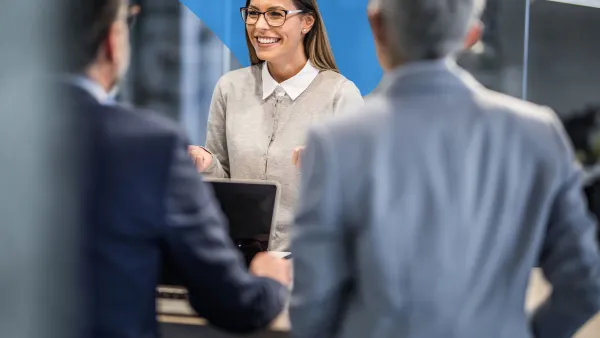 Three professionals working together at a computer, smiling and reviewing lines of code displayed on a large screen.
