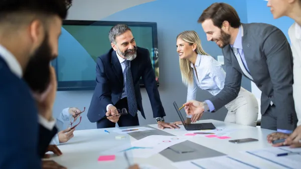 Business professionals in a meeting, collaborating and discussing strategy around a table covered with charts and documents.