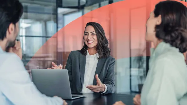 Smiling businesswoman leading a discussion with colleagues around a laptop during a meeting.