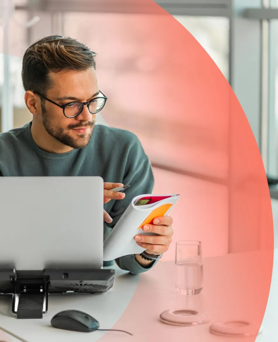 Professional working at a desk with a laptop and notebook and reviewing notes in a notebook.